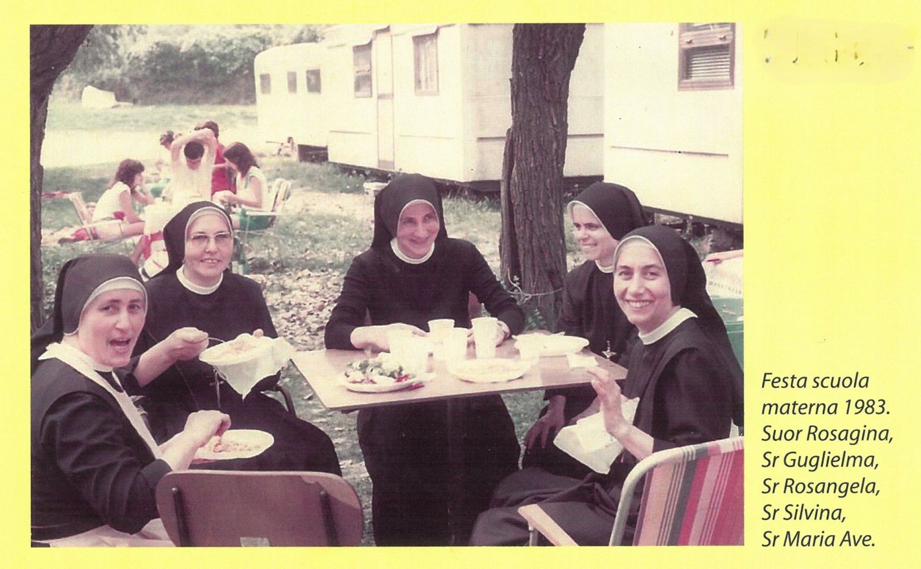 Donne in abiti neri siedono a tavoli all'aperto accanto a un edificio, sorridendo e mangiando insieme.