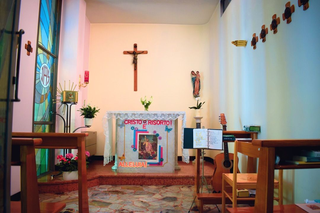 Piccolo altare in una chiesa con crocifisso in legno, candele e panche, all'interno di una semplice cappella.