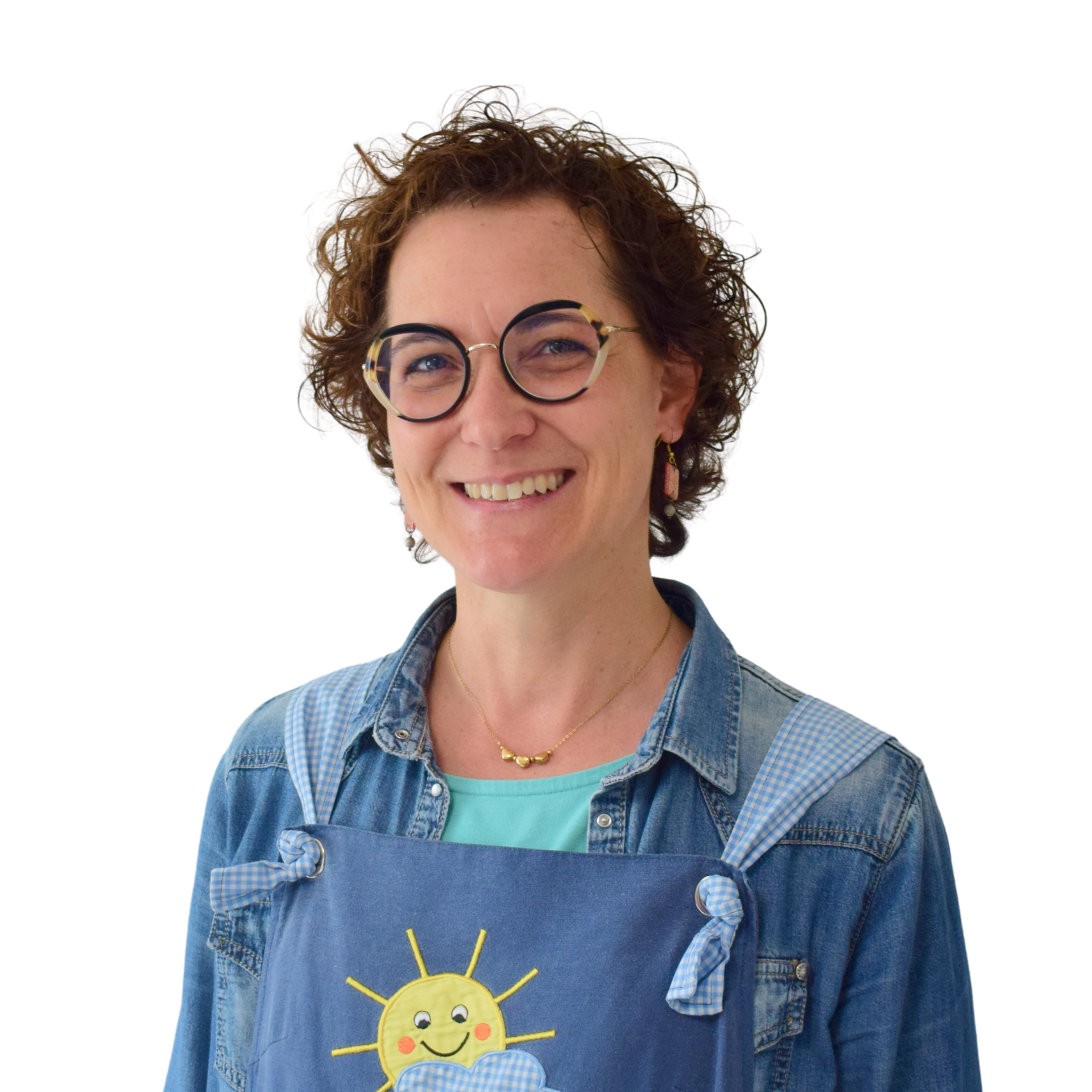 Persona sorridente con capelli ricci, occhiali rotondi e camicia di jeans sopra una maglietta blu, in piedi su uno sfondo bianco.