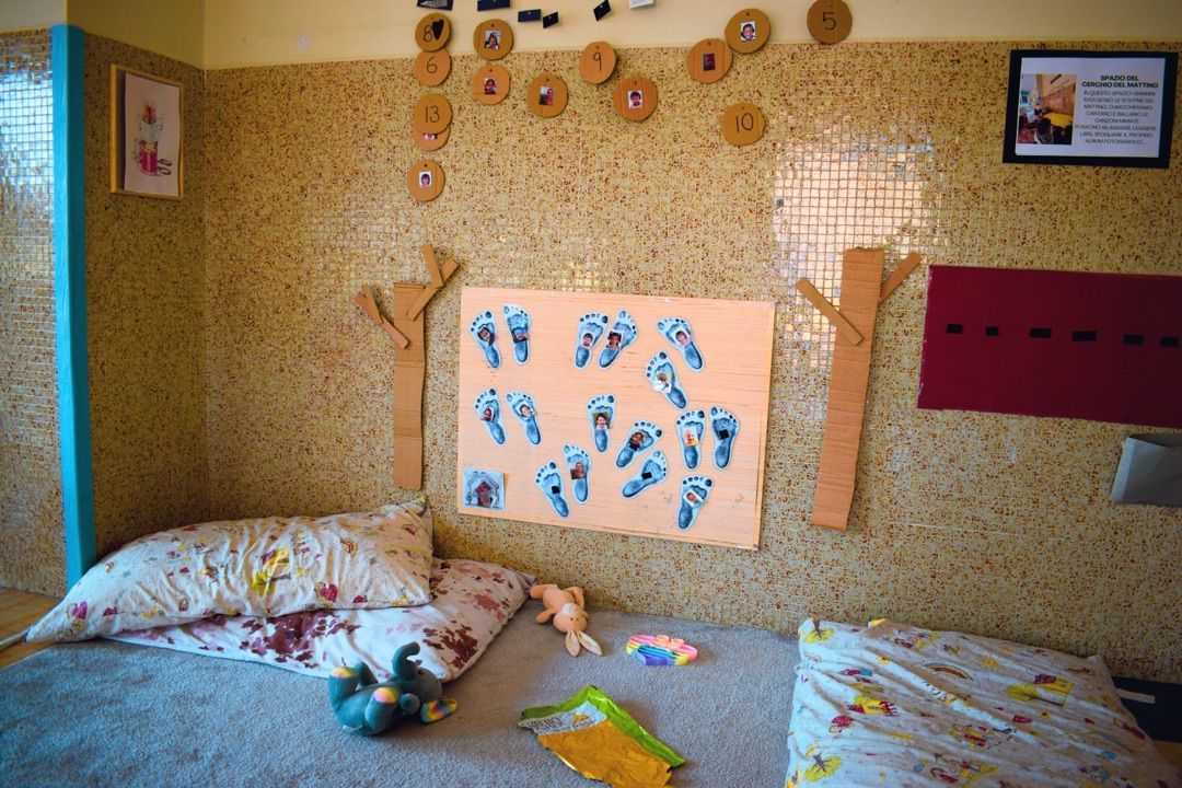 Parete della cameretta del bambino decorata con disegni a forma di impronte di mani, cuscini sul letto e un piccolo paravento incorniciato sulla destra.