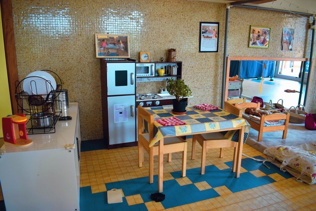 Accogliente cucina-sala da pranzo con pavimento a scacchi, tavolo in legno, scaffali e frigorifero.