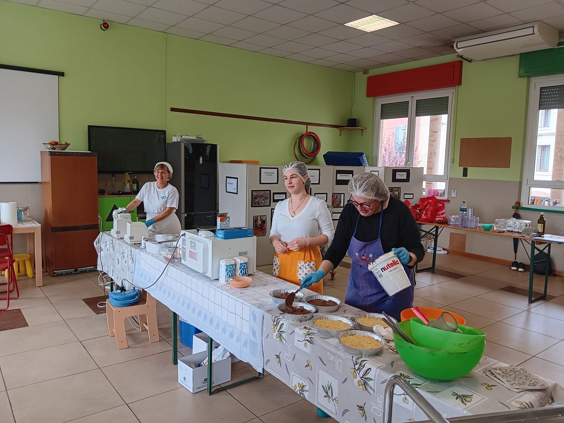 Persone che preparano il cibo a un tavolo in una stanza luminosa, con ciotole e utensili da cucina sparsi ovunque.