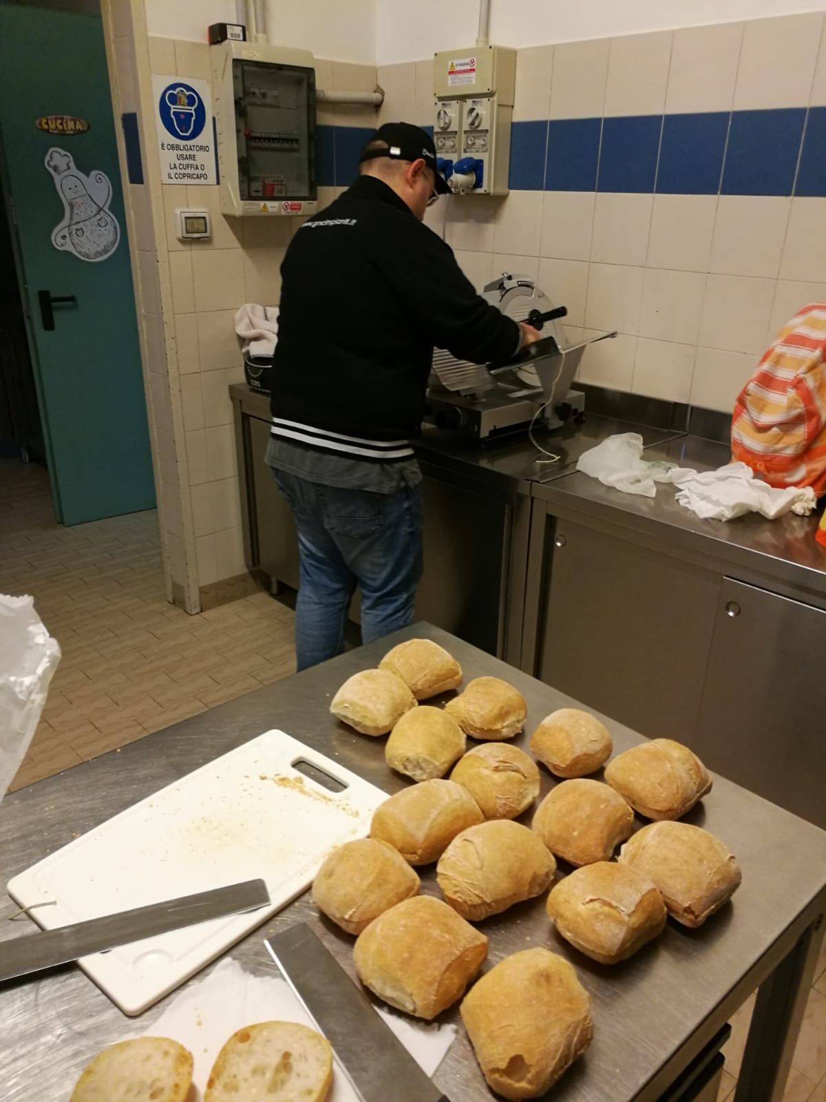 Una persona in cucina maneggia del cibo, con un vassoio di panini su un bancone.