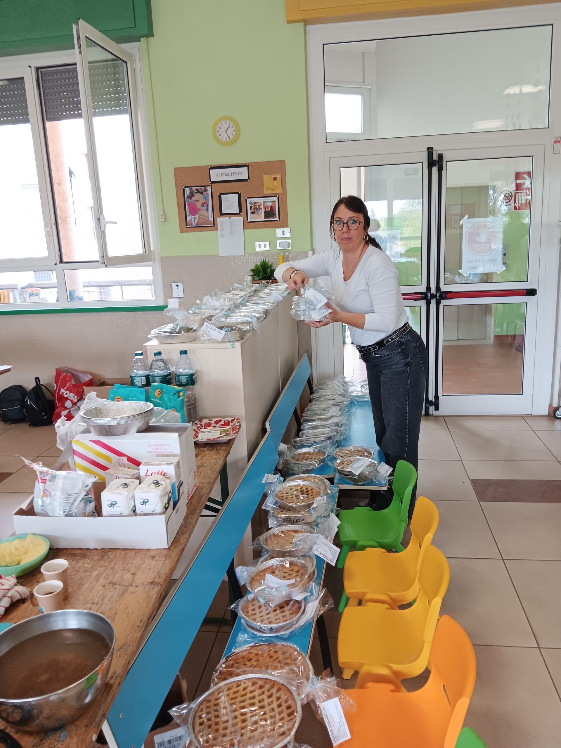 Una donna sistema il cibo su un lungo tavolo in una luminosa sala comunale.