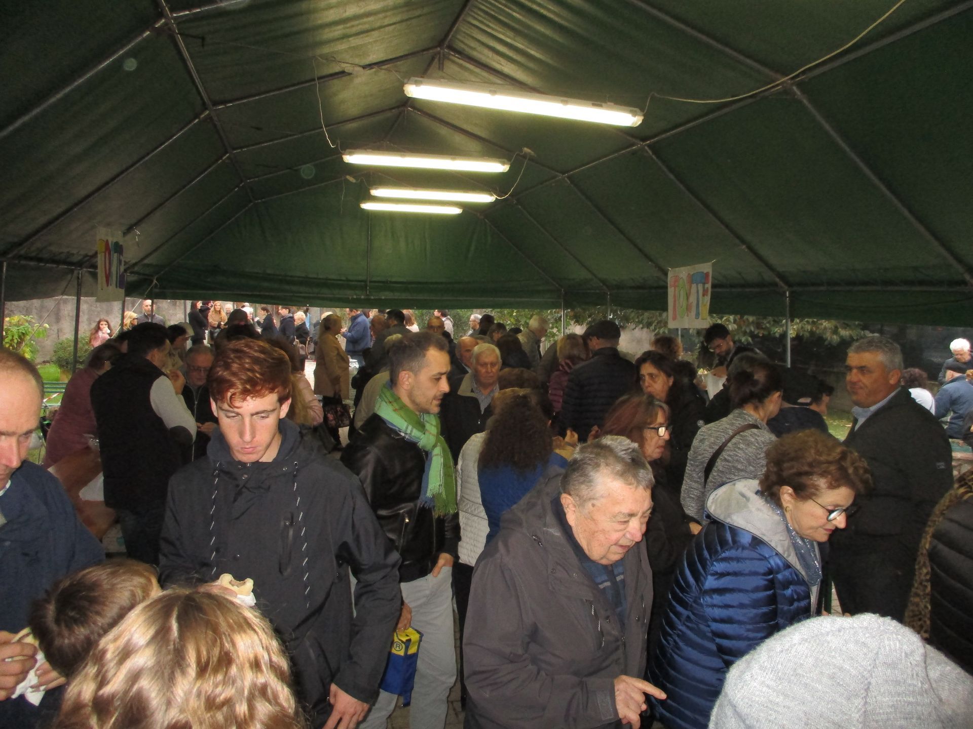 Un tendone del mercato affollato, con persone che curiosano sotto luci verdi.