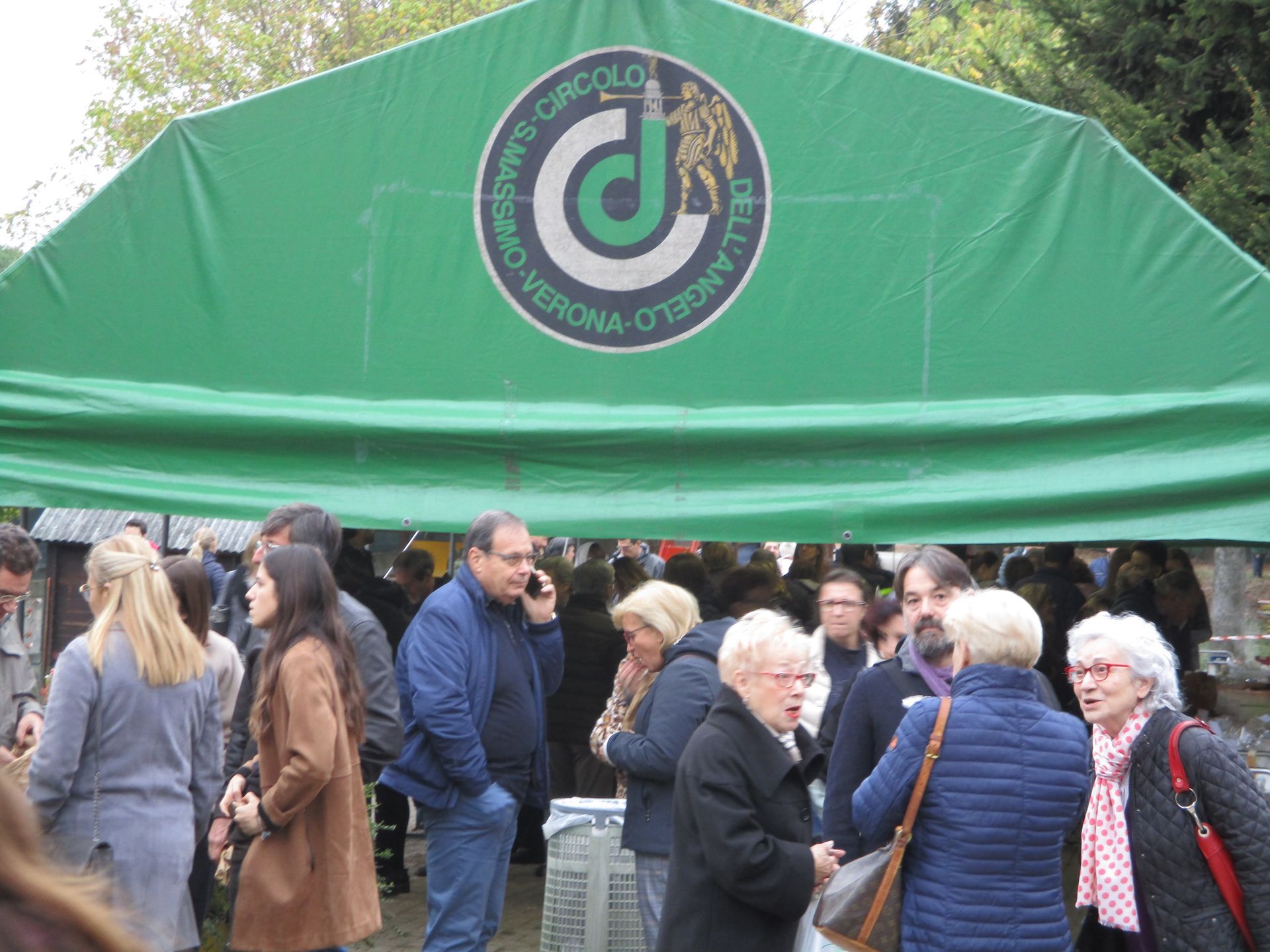 Durante un evento all'aperto, diverse persone si sono riunite sotto un tendone verde con un logo circolare.