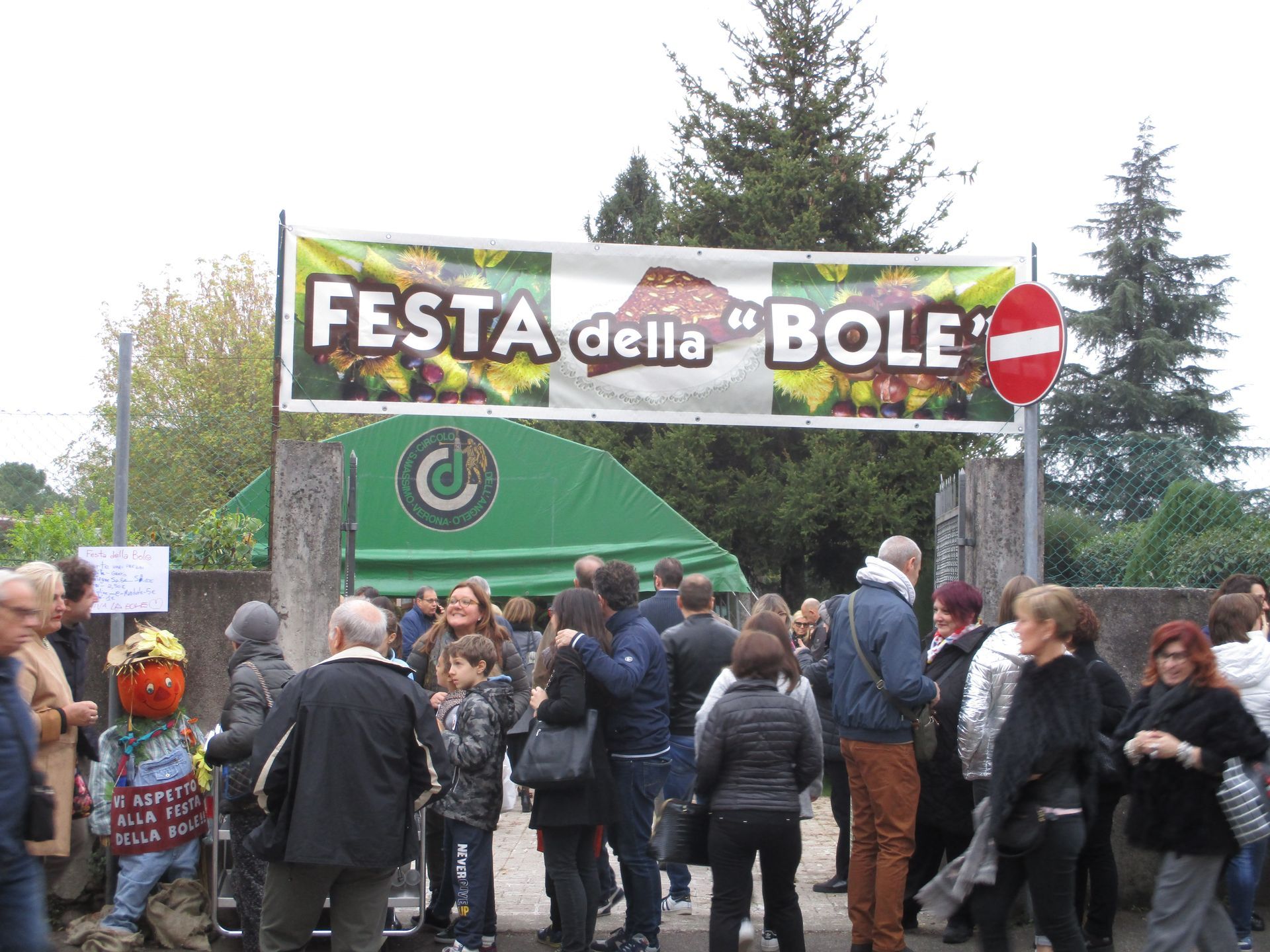 Folla radunata presso lo striscione d'ingresso della Festa della Bole, con alberi sullo sfondo.