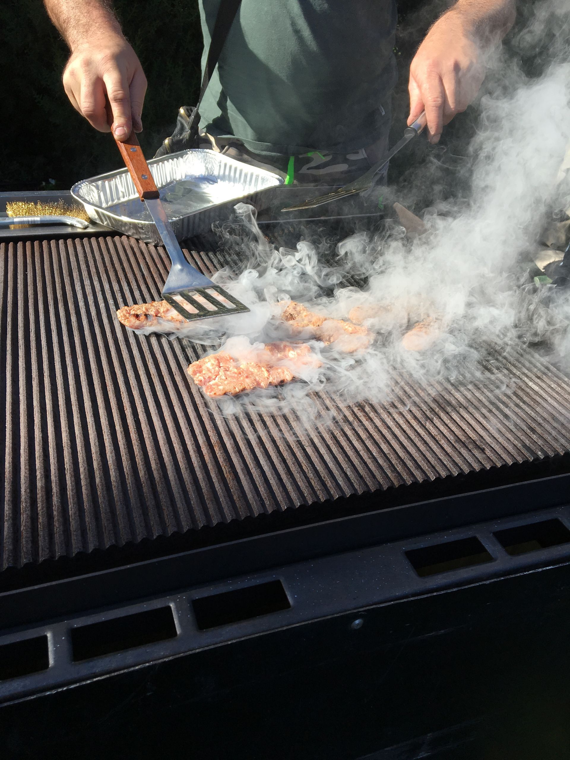 Mani che grigliano la carne su un barbecue fumante con pinze e spatola
