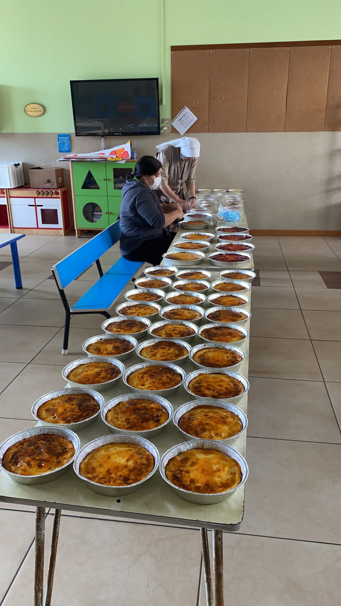 In un'aula scolastica, file di piatti di cibo disposti su lunghi tavoli, con una persona seduta all'estremità opposta.