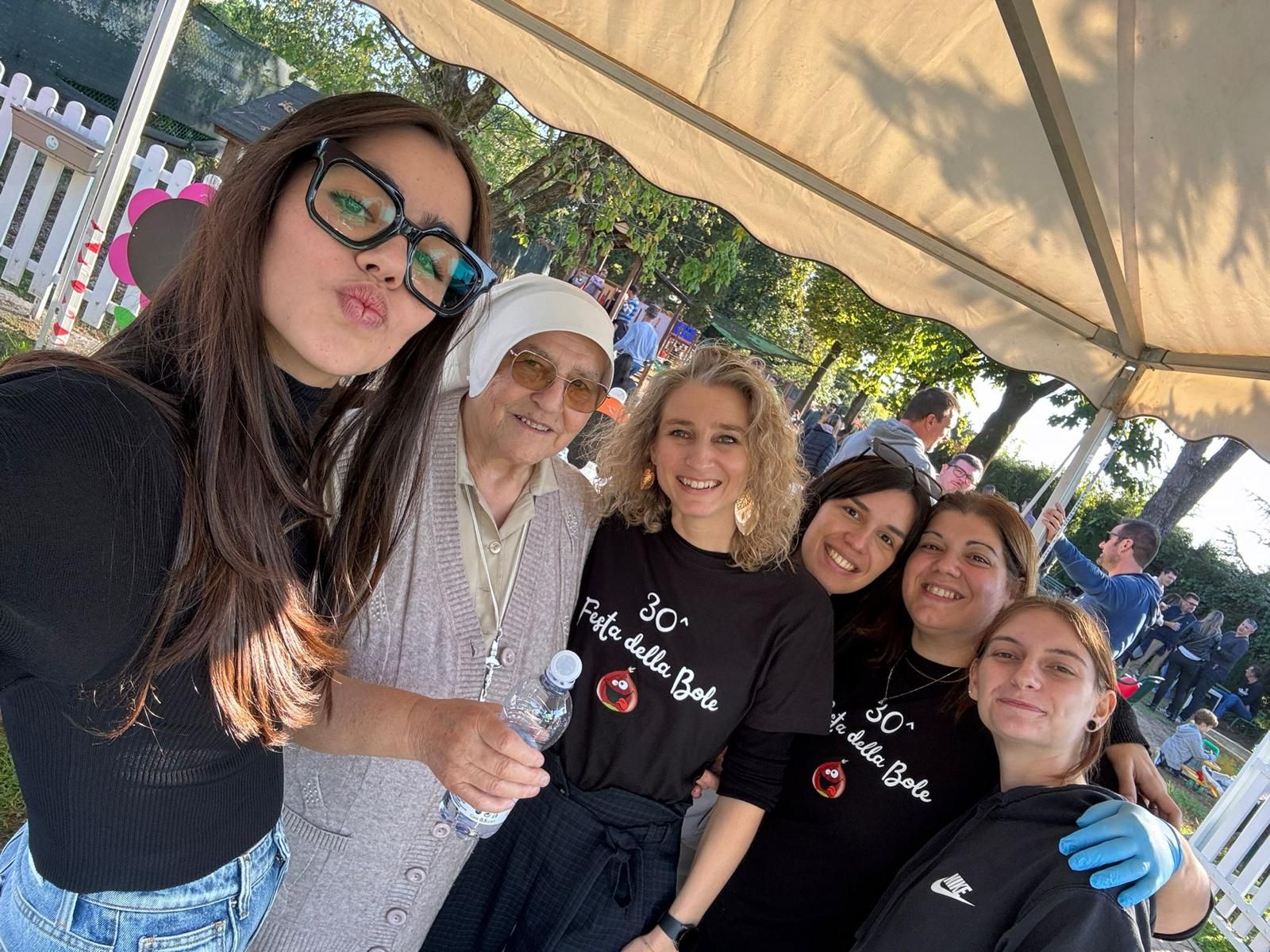 Gruppo di sei amici sorridenti in posa all'aperto sotto una tettoia durante un evento.