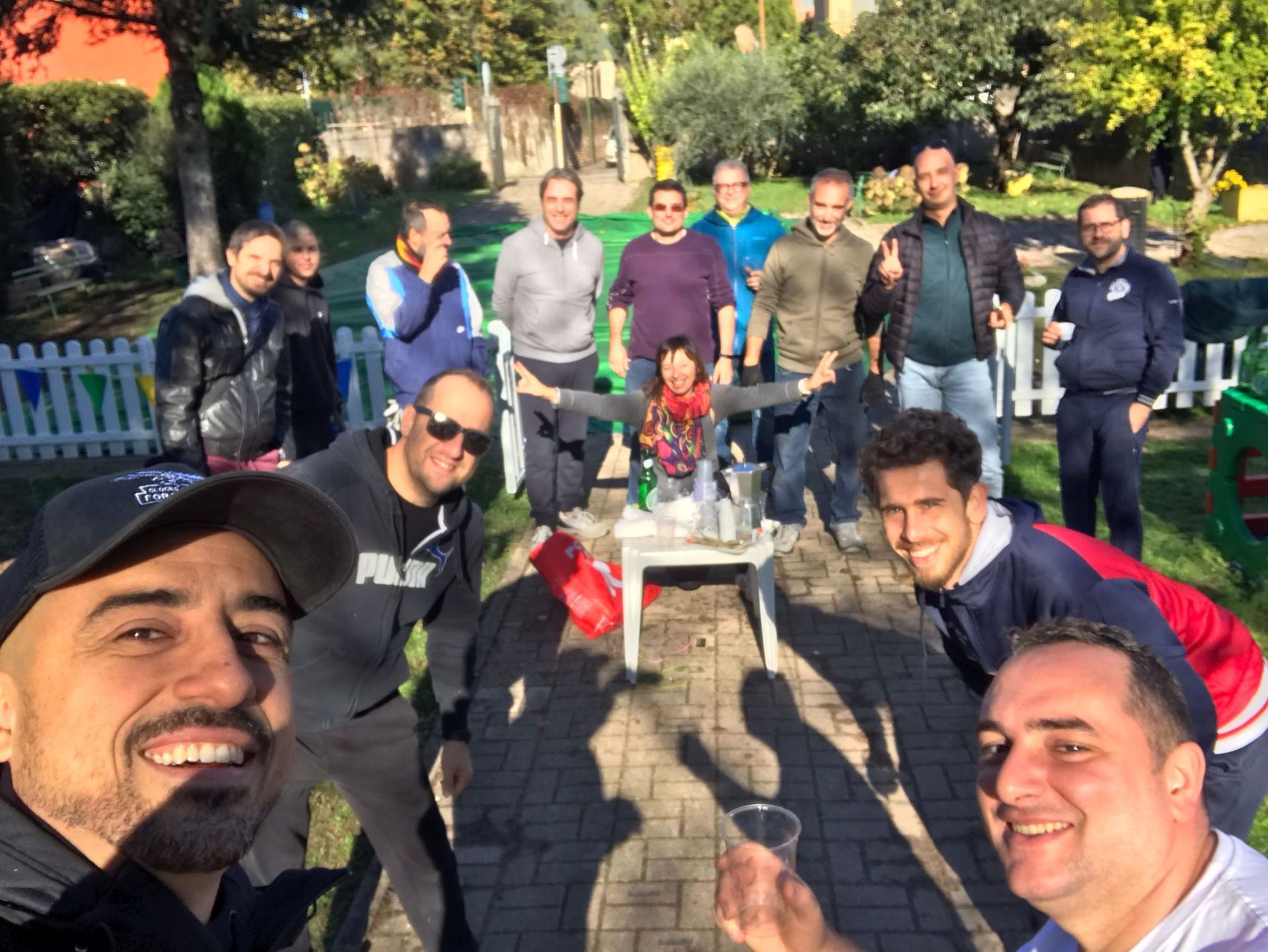 Un gruppo di amici posa all'aperto in un parco soleggiato, sorridendo attorno a un tavolo con bevande e snack.