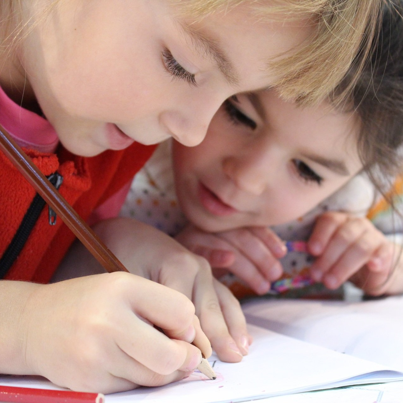 Due bambini chinati su un quaderno, disegnano insieme con le matite colorate.