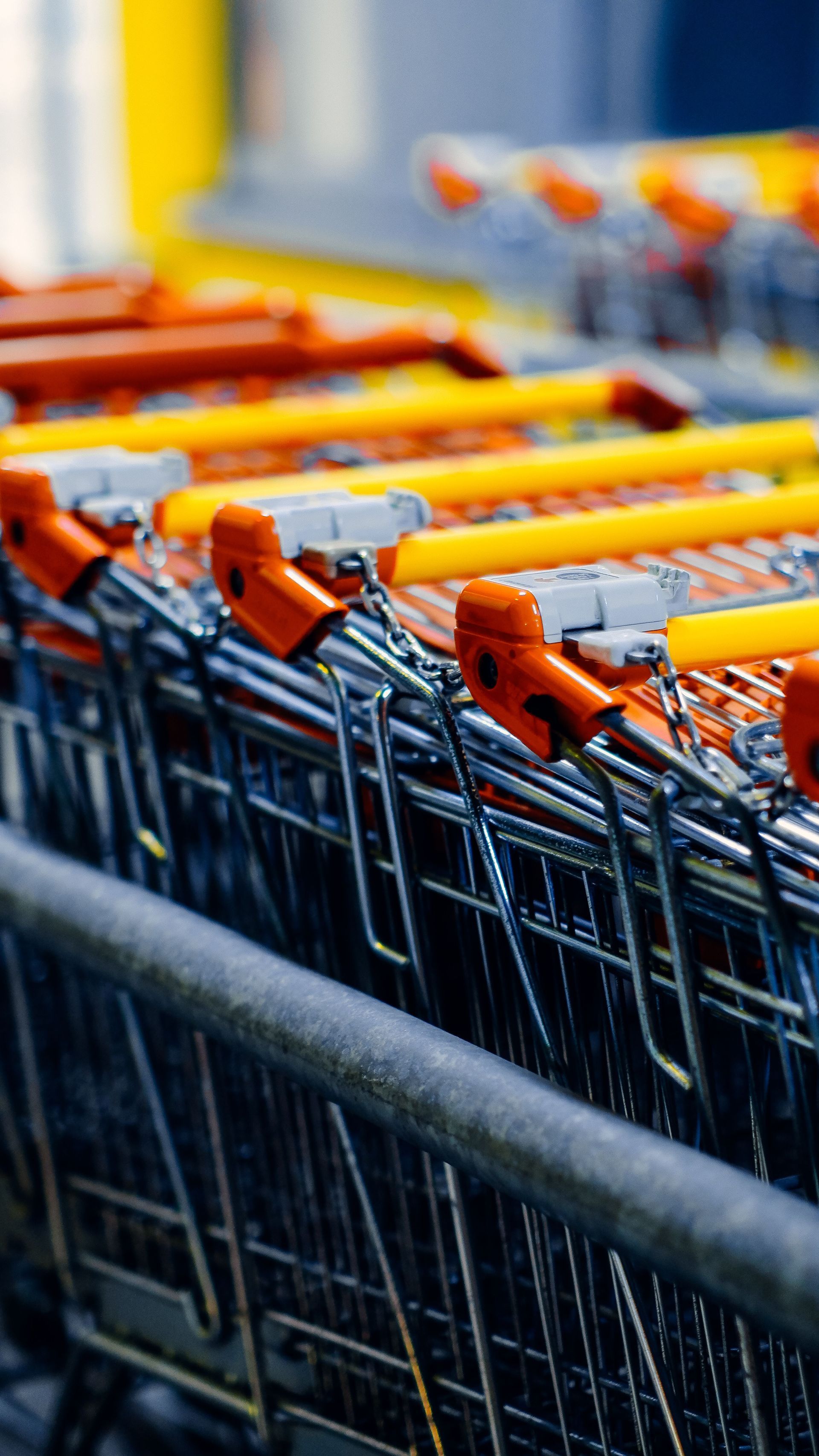 Rows of nested shopping carts with orange handles in a store parking area