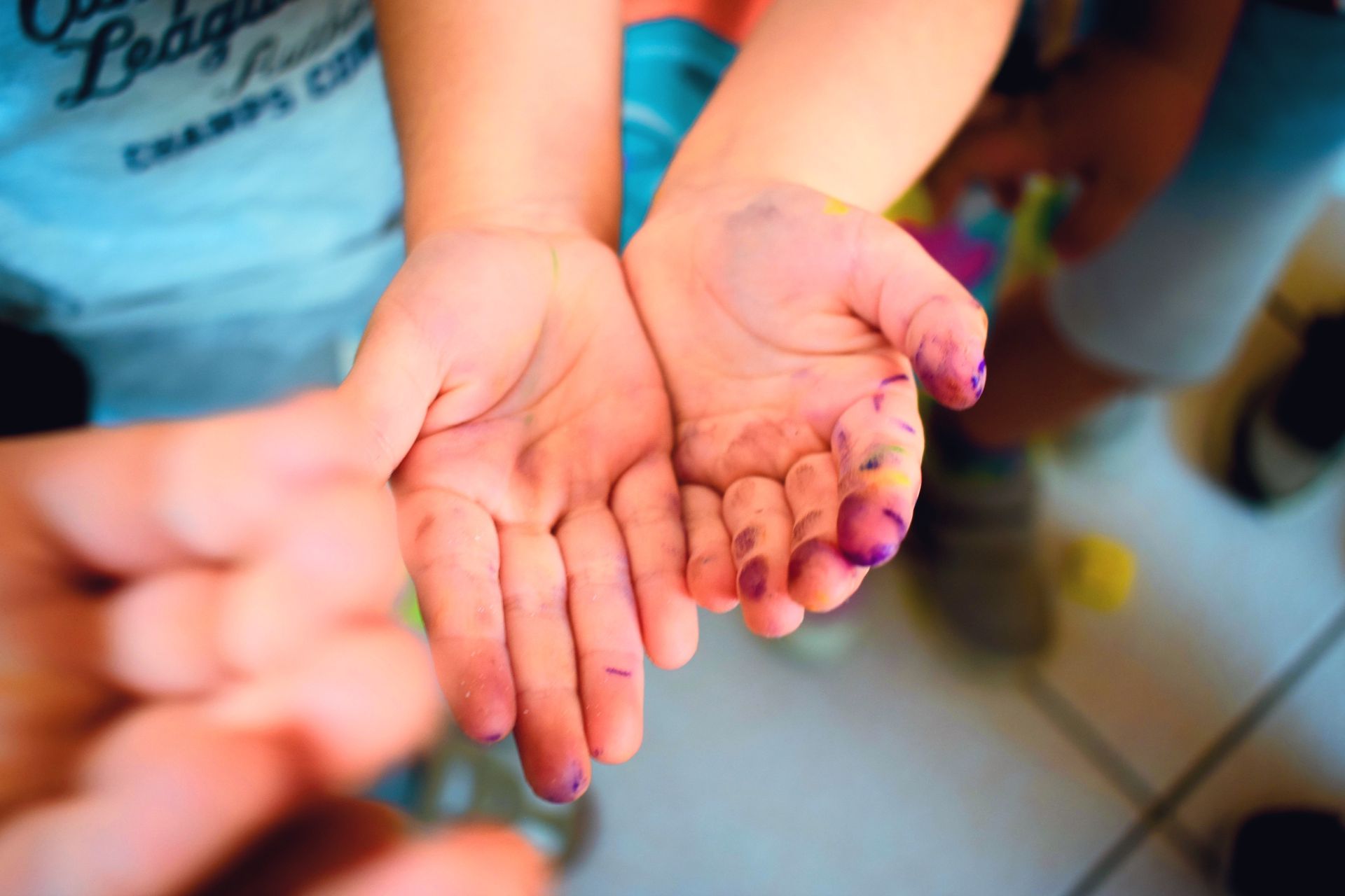 Mani aperte a coppa, una delle quali regge piccoli oggetti, in un ambiente interno colorato.