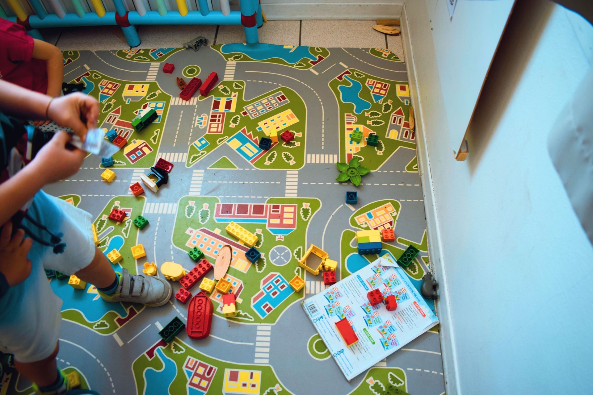 Un bambino gioca con macchinine colorate su un tappeto da gioco in una stanza luminosa, con giocattoli sparsi tutt'intorno.