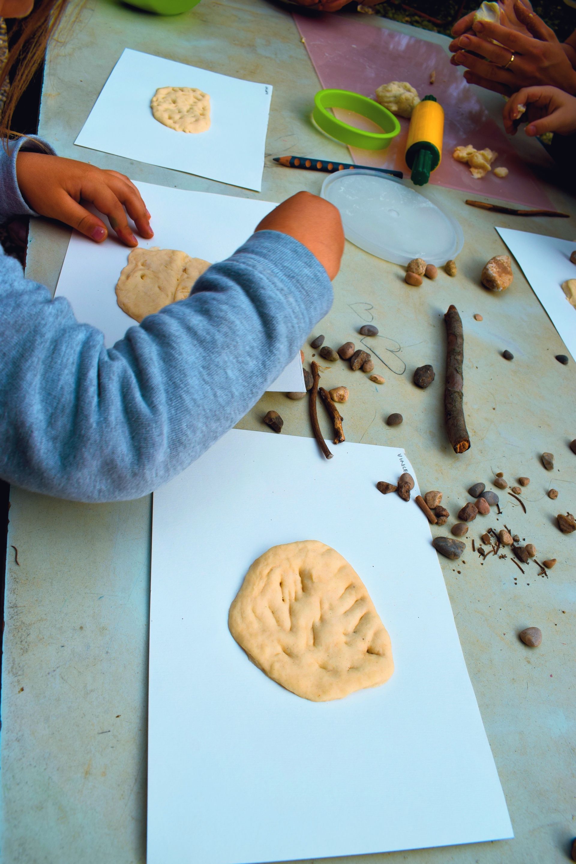 Bambini che creano opere d'arte con l'argilla su carta bianca seduti a un tavolo, con strumenti e pezzetti di argilla sparsi.