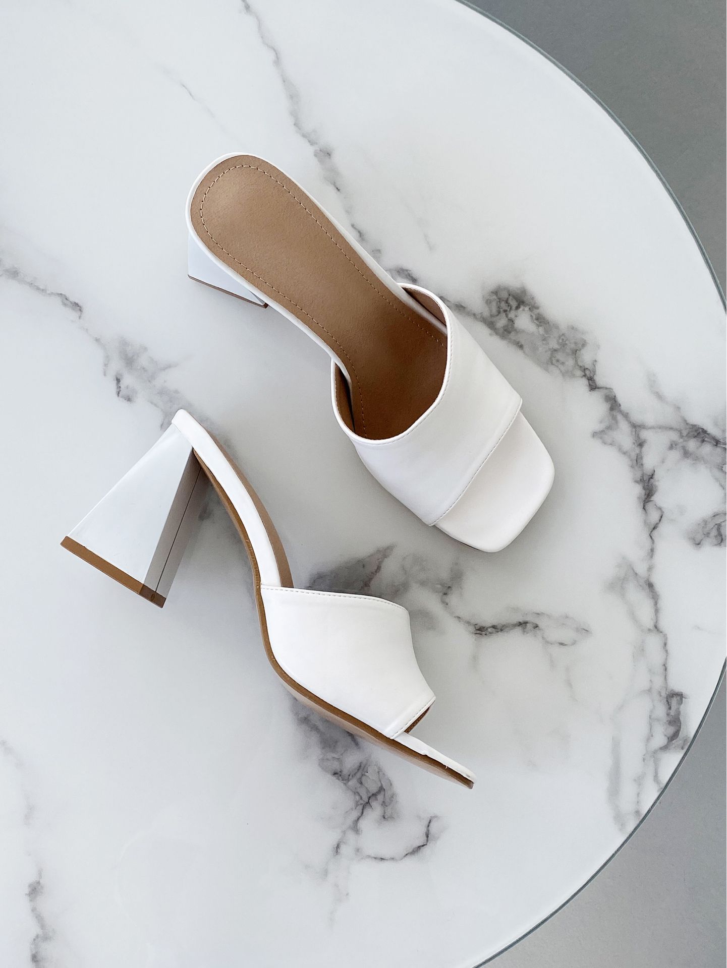 Witte leren sandalen met hakken op een marmeren ondergrond.