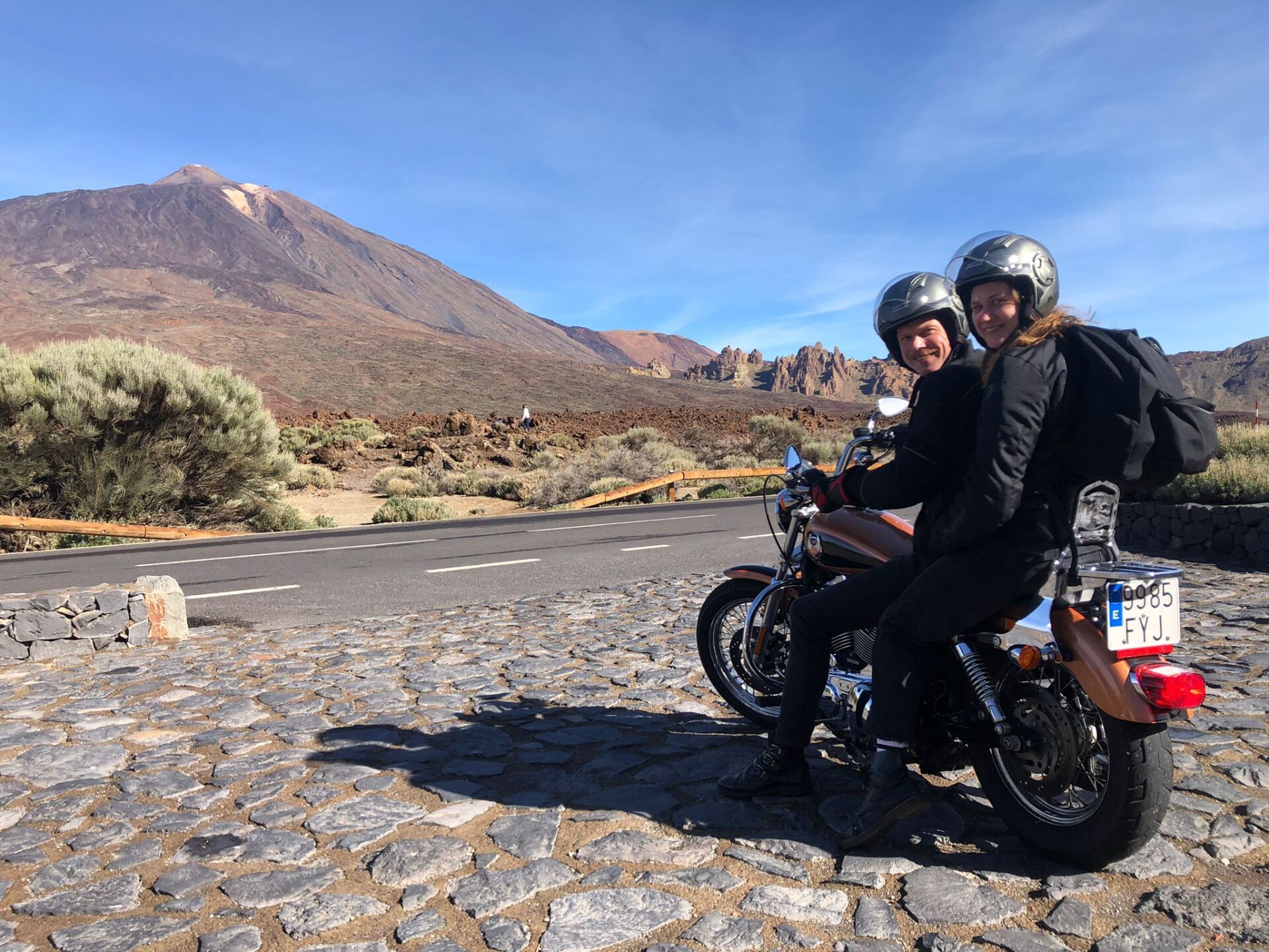 Two people are riding a motorcycle on a cobblestone road.