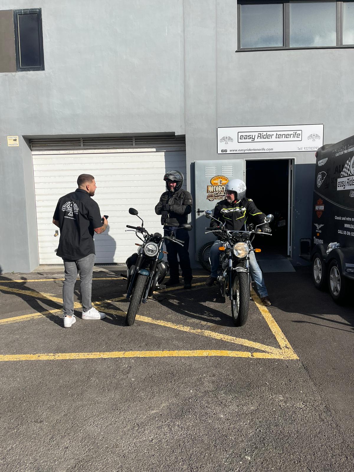 A group of people standing next to motorcycles in a parking lot.