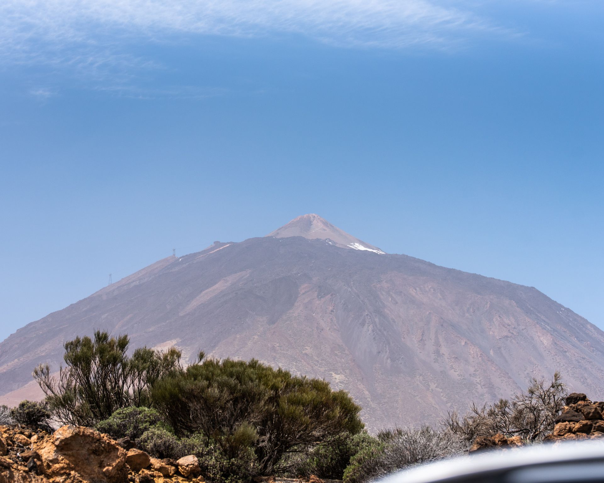 A mountain with trees in the foreground and a blue sky in the background