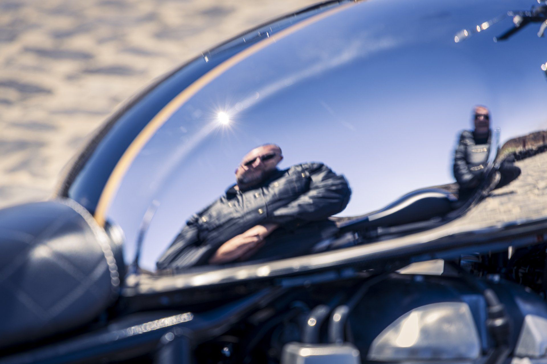 A man is reflected in the tank of a motorcycle.