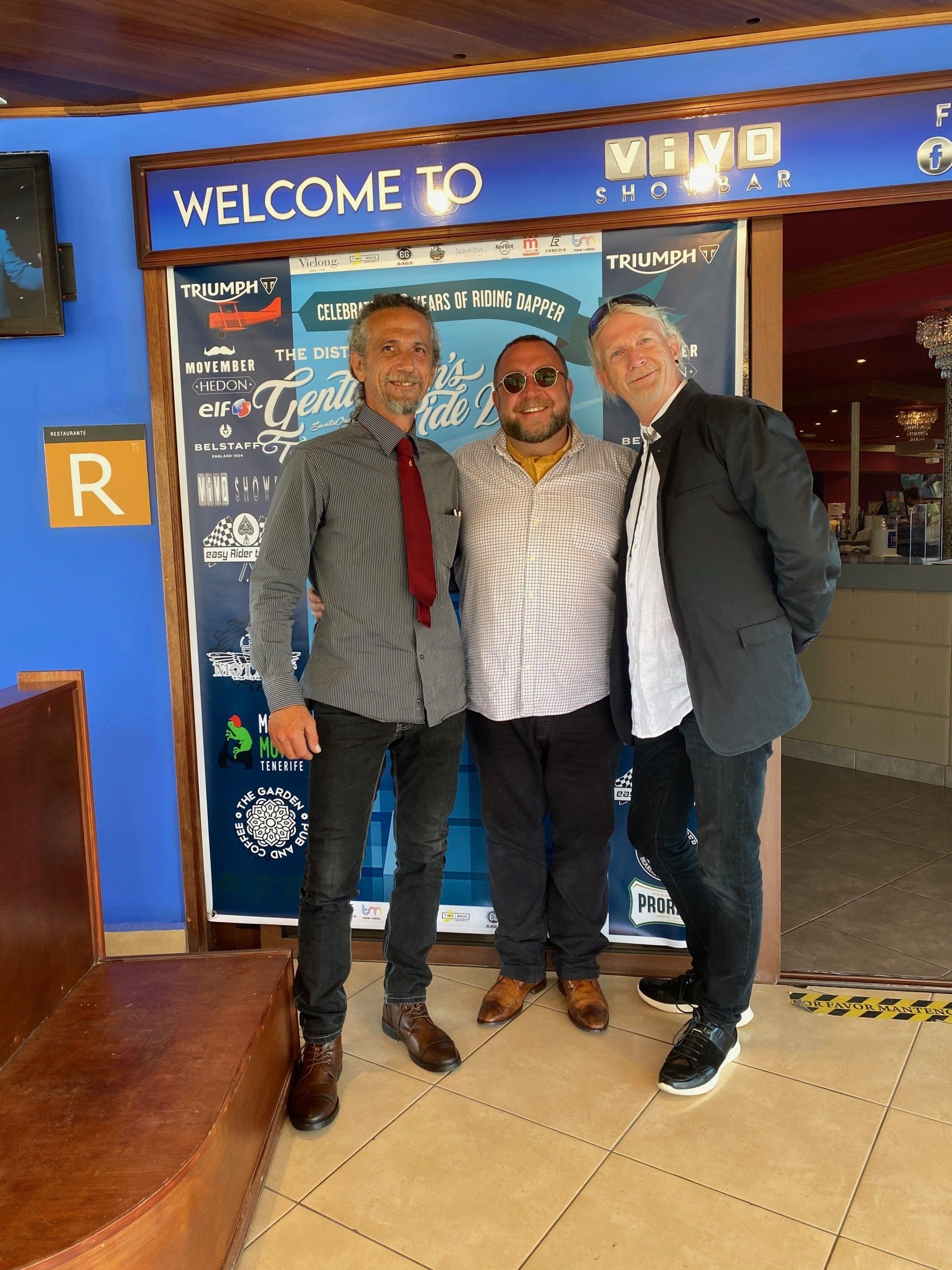 Three men are posing for a picture in front of a welcome sign