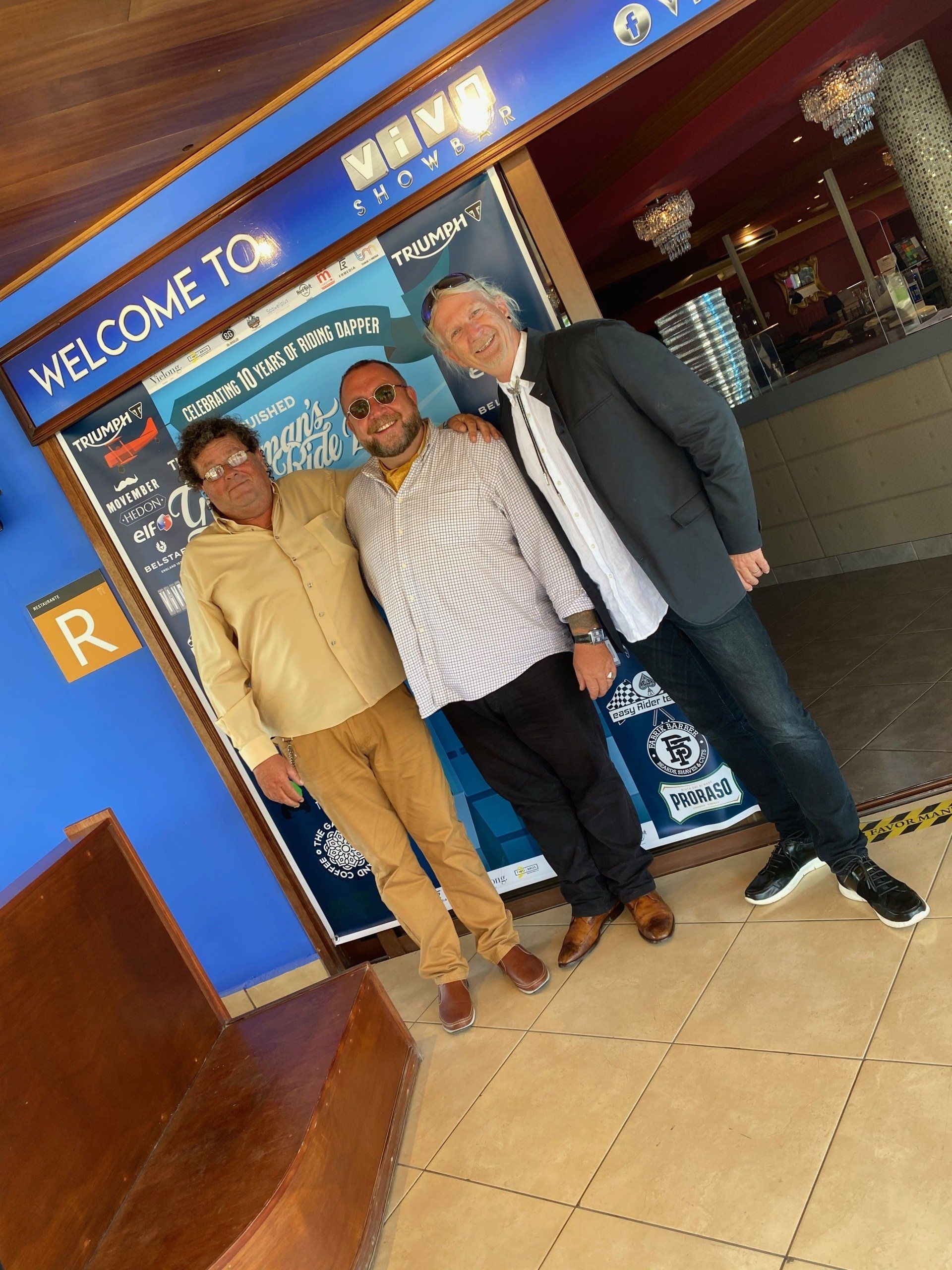 Three men are posing for a picture in front of a welcome sign.