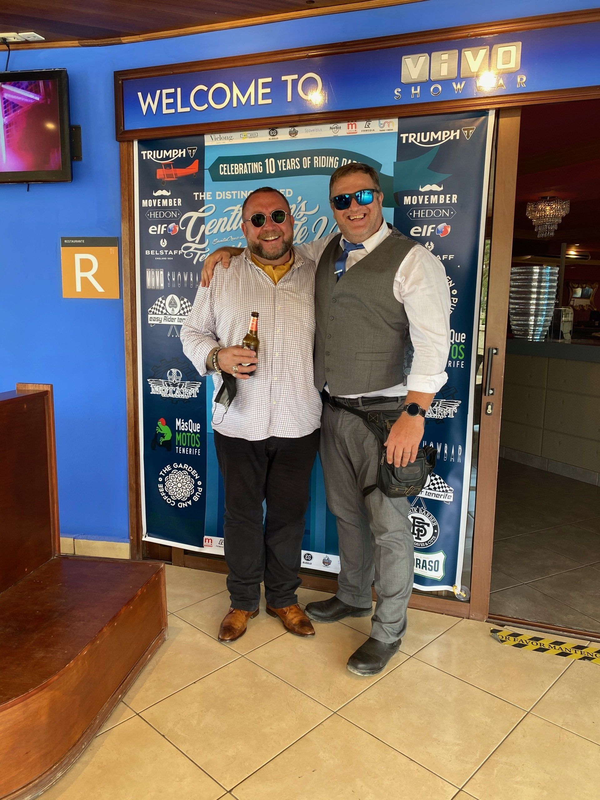 Two men are posing for a picture in front of a welcome sign