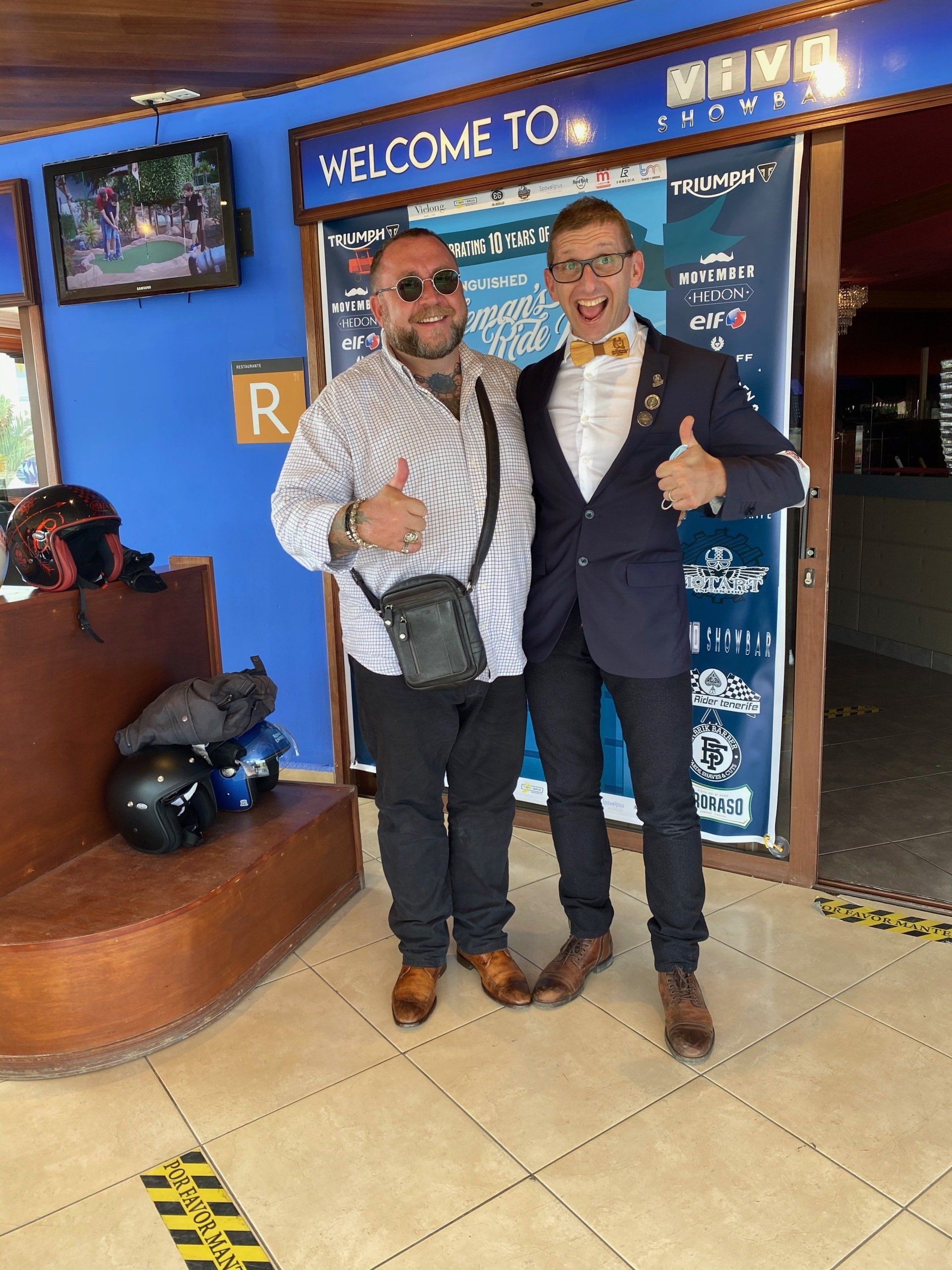 Two men are posing for a picture in front of a welcome sign.