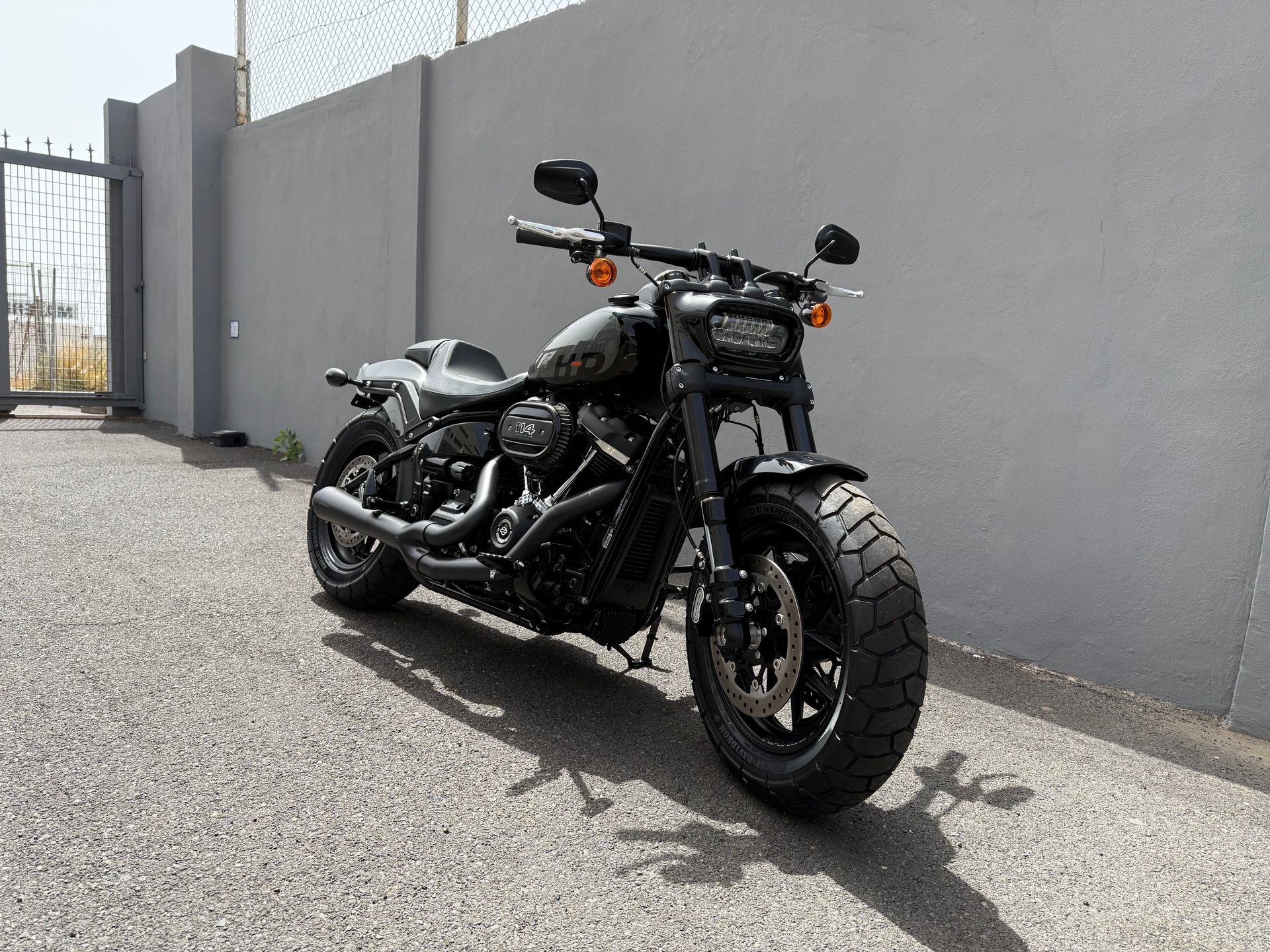 Black Harley-Davidson motorcycle for rent parked on gravel next to a gray wall.