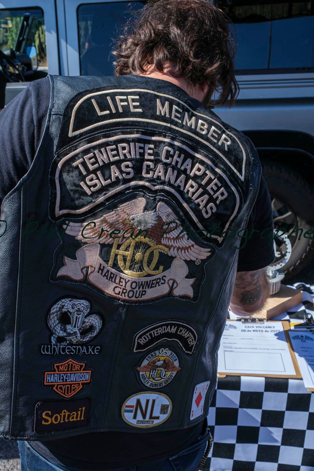 A man wearing a black leather vest with a lot of patches on it.