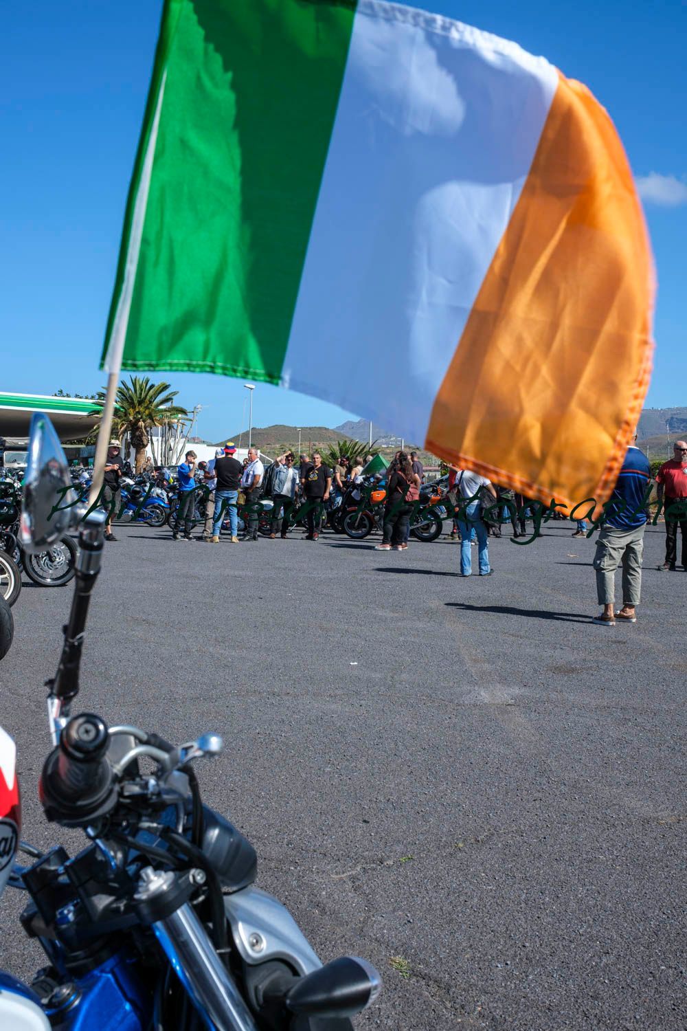 A green , white and orange flag is hanging from the handlebars of a motorcycle.