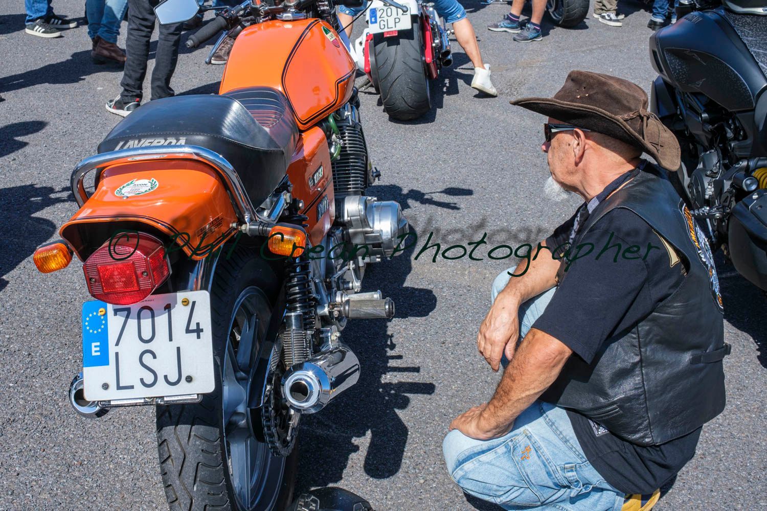 A man is kneeling in front of an orange motorcycle with a license plate that says 7014 lsj