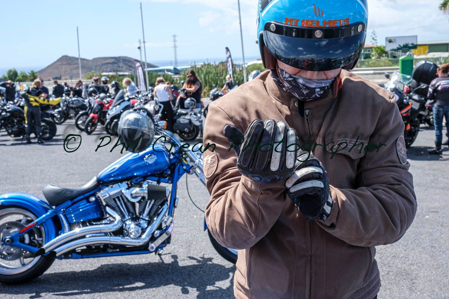 A man wearing a helmet and gloves is standing in front of a blue motorcycle.