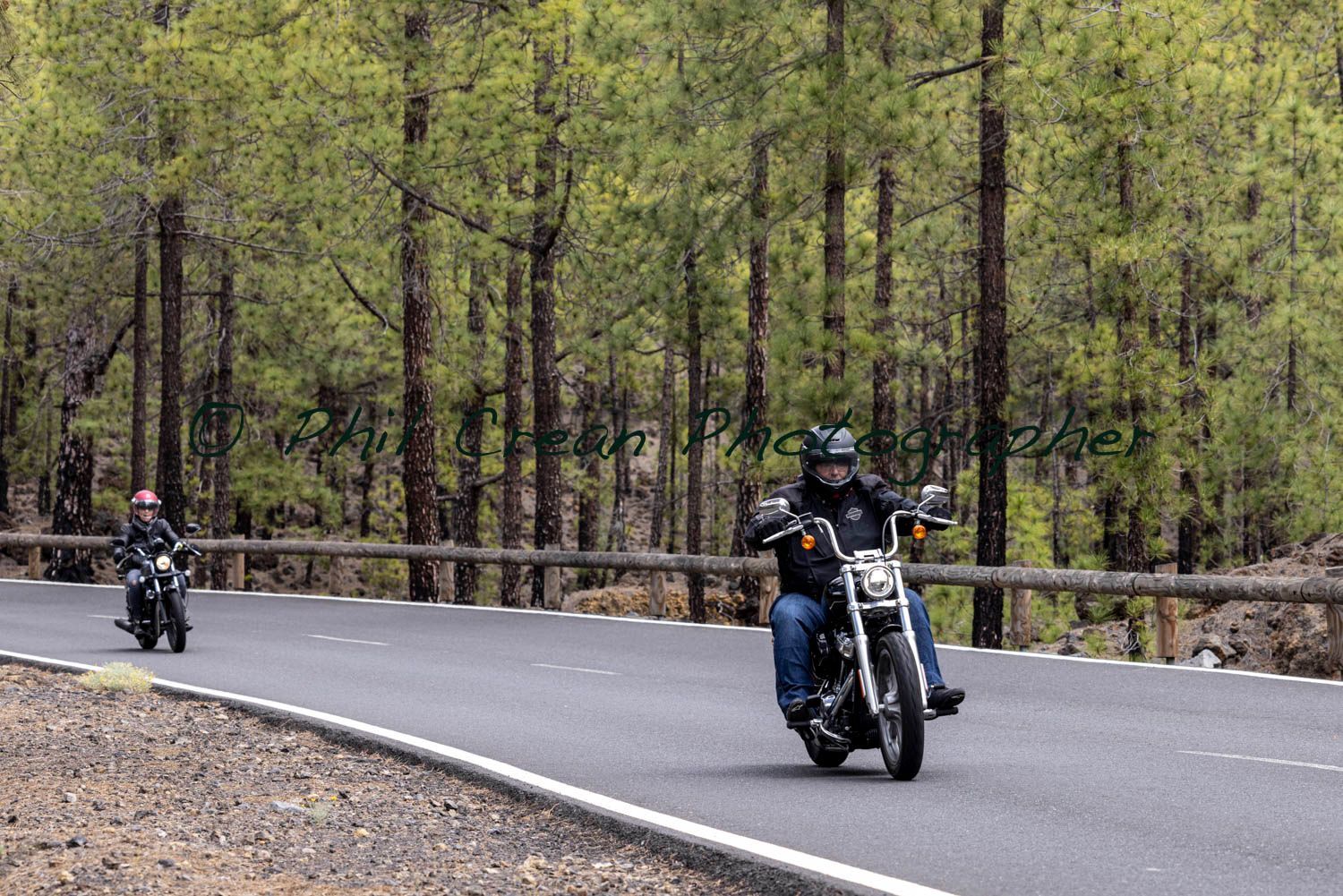 Two men are riding motorcycles down a road in the woods.
