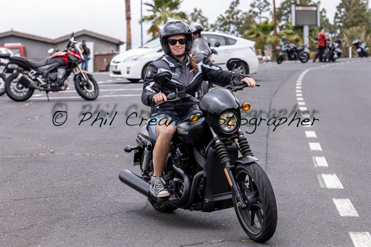 A woman is riding a motorcycle down a street.