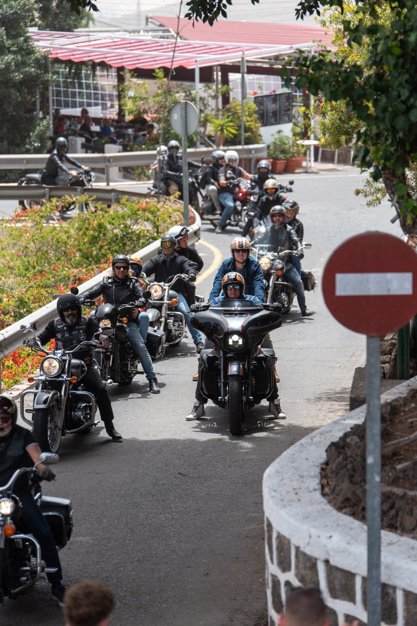 A group of people riding motorcycles down a street with a no entry sign