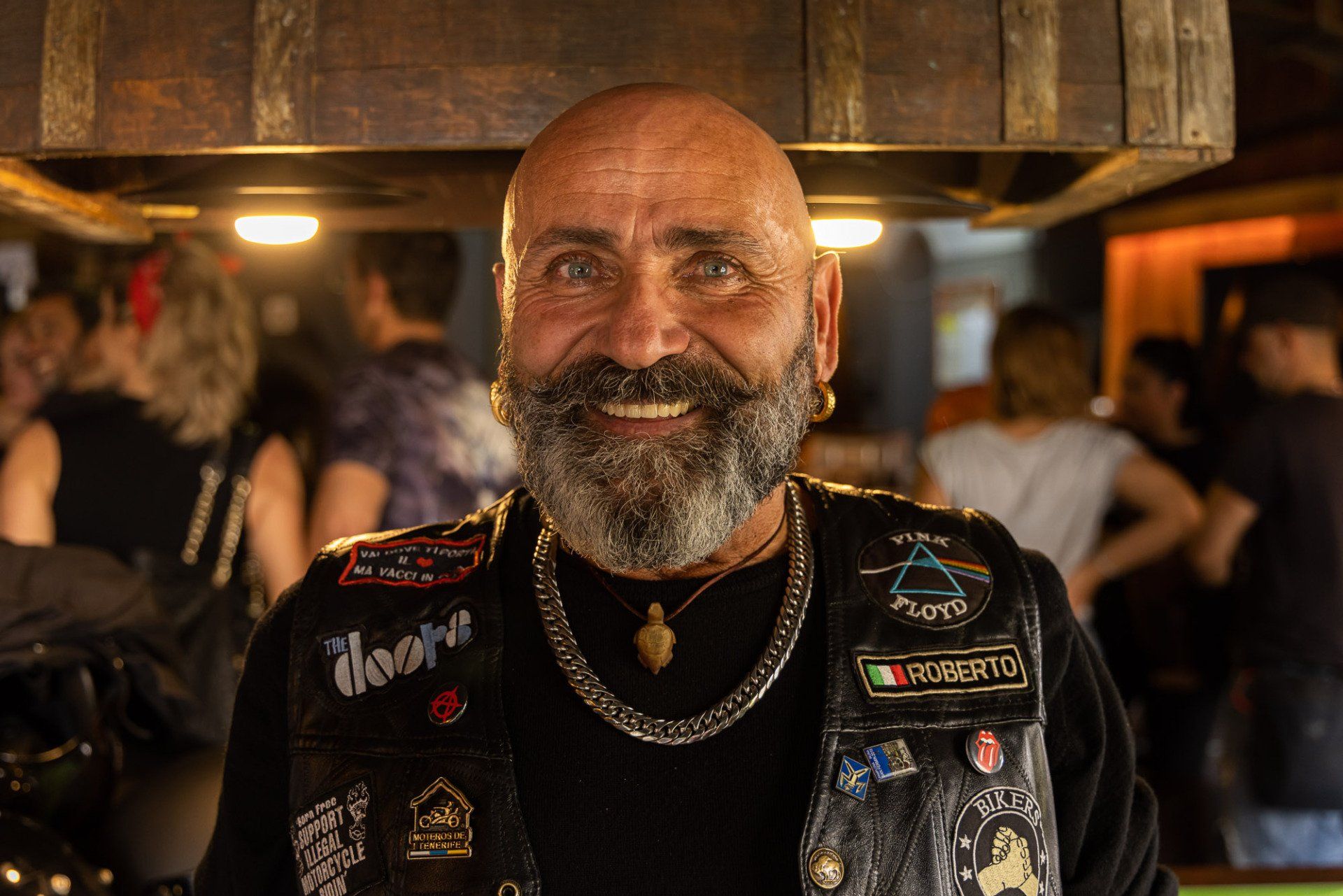 A man with a beard is wearing a black vest with patches on it.