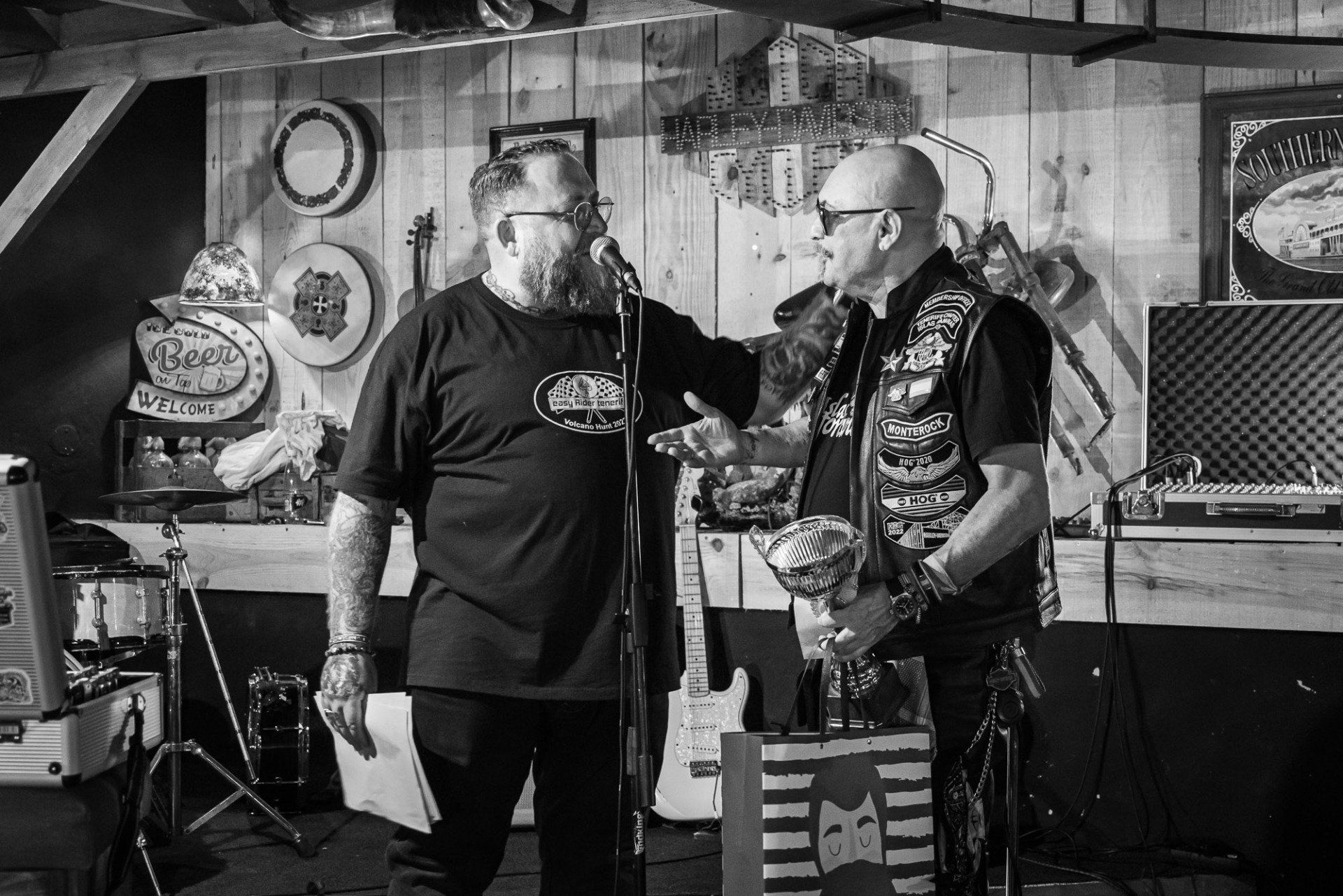 Two men are standing in front of a microphone in a black and white photo.
