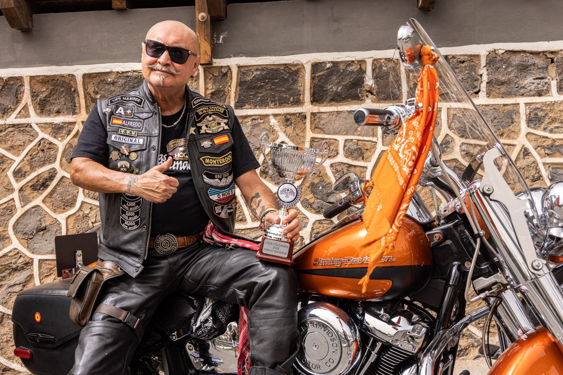 A man is sitting on a motorcycle in front of a stone wall.