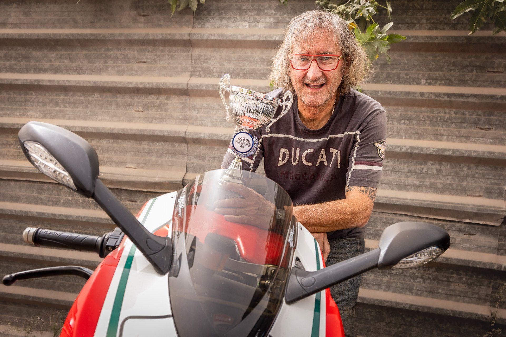 A man wearing a ducati shirt is standing next to a motorcycle.