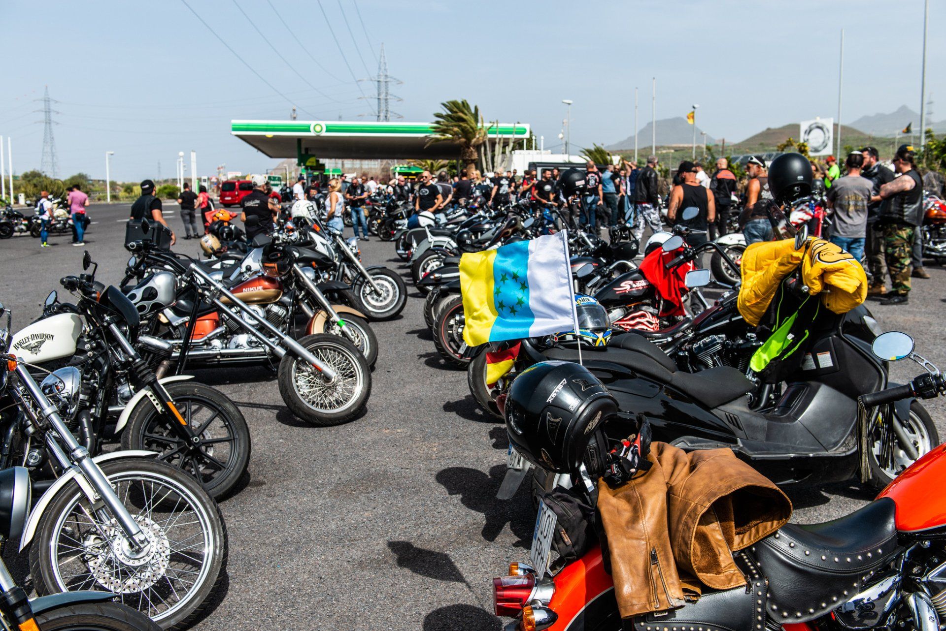 A lot of motorcycles are parked in a parking lot in front of a gas station.