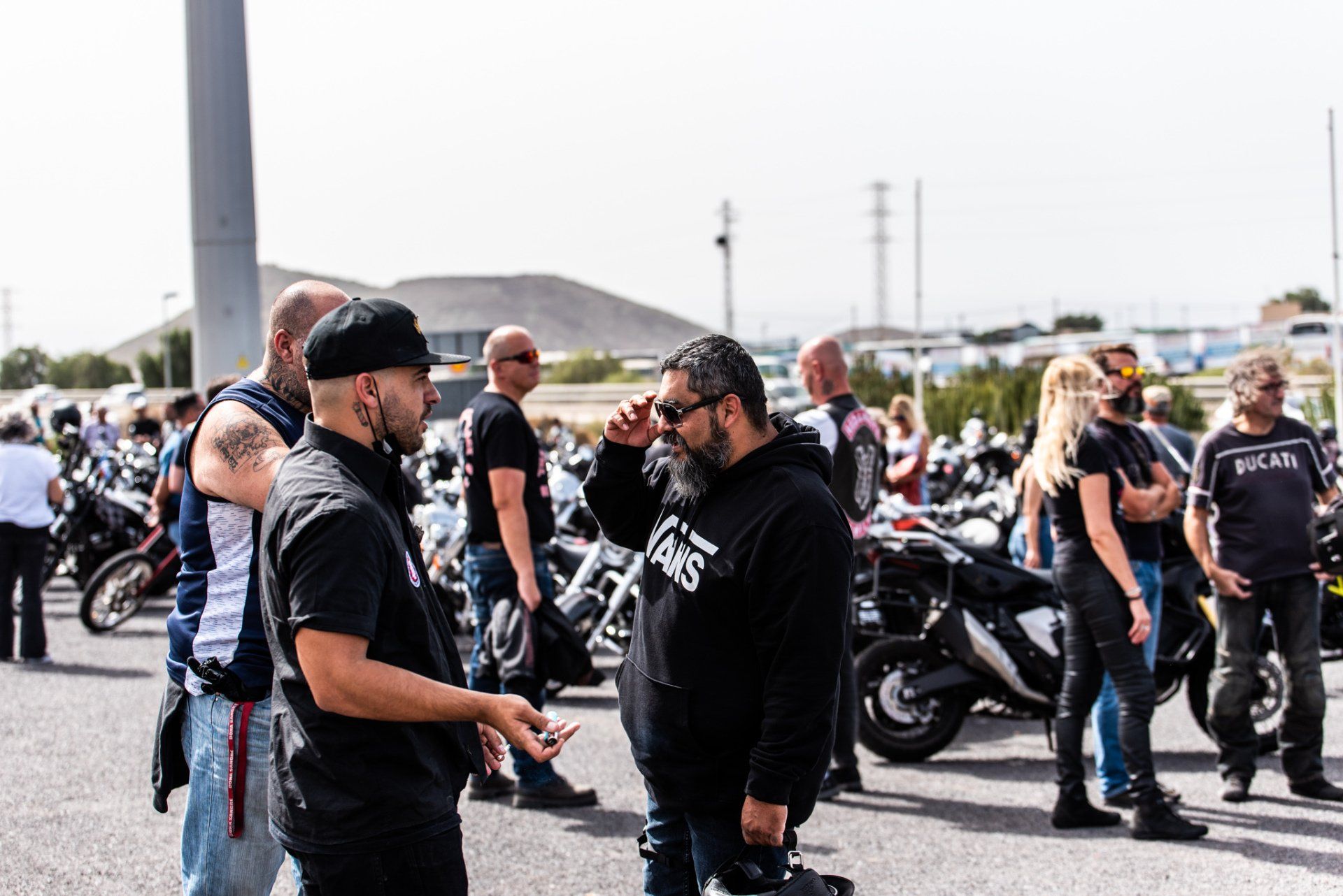 A group of motorcycle riders are standing in a parking lot talking to each other.