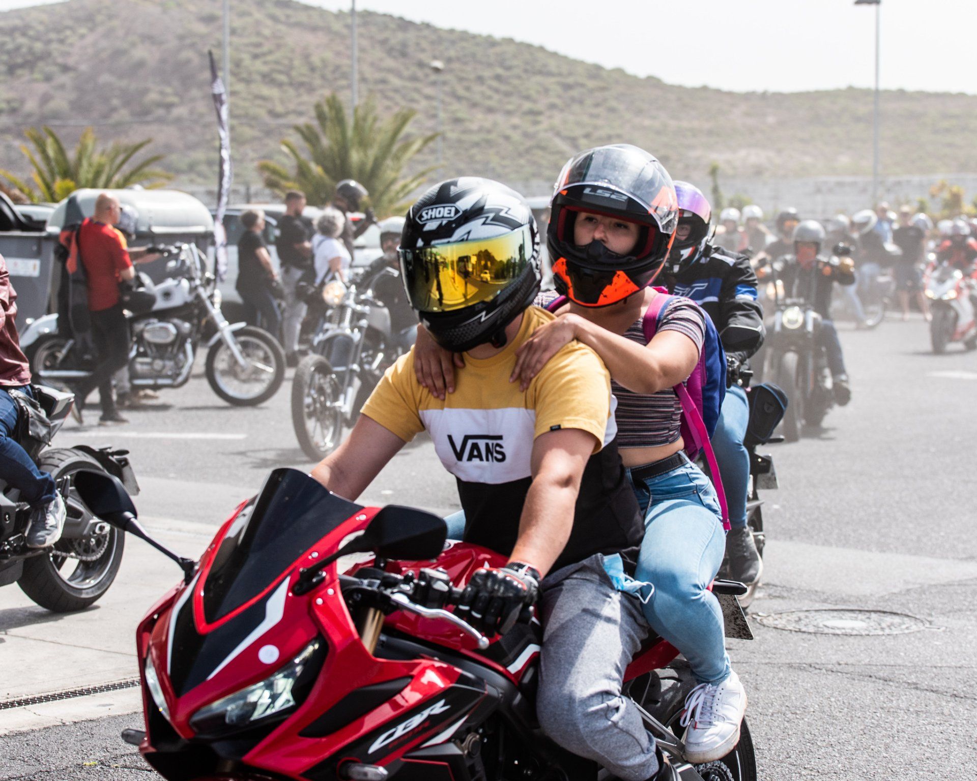 A man wearing a vans shirt is riding a motorcycle with a woman on his back.
