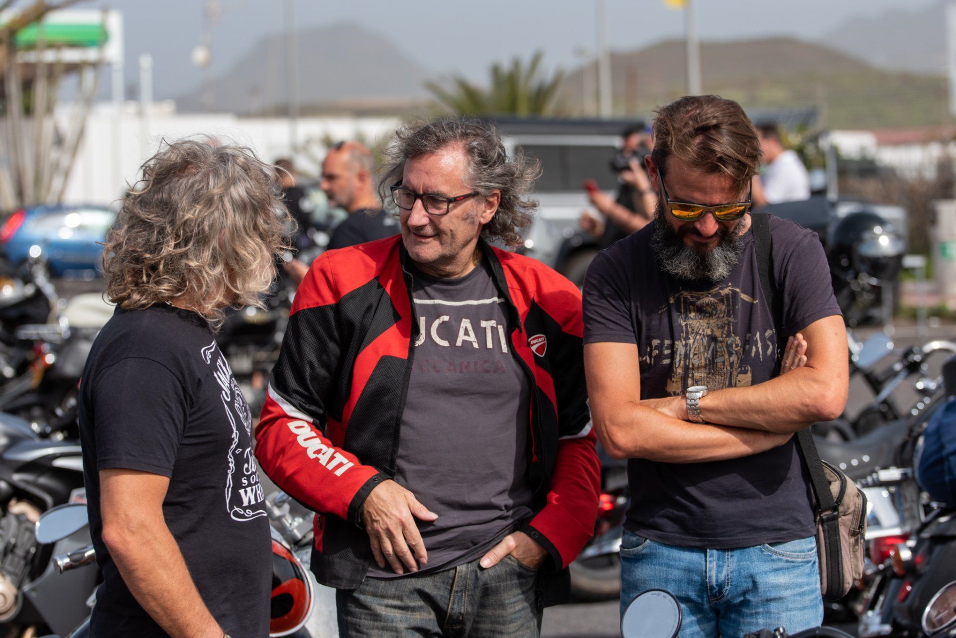 Three men are standing next to each other in a parking lot talking to each other.