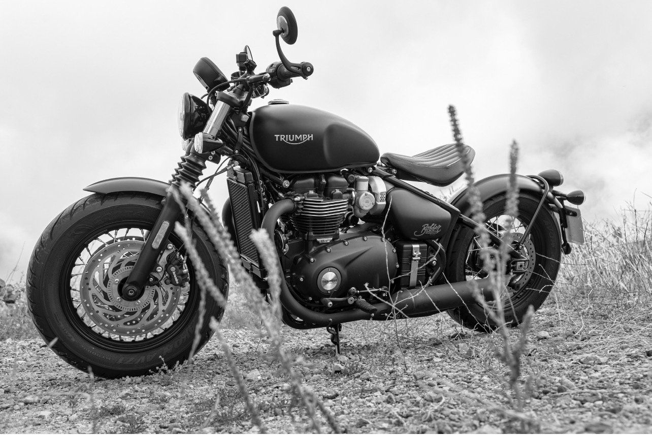 A black and white photo of a motorcycle parked on top of a dirt hill.