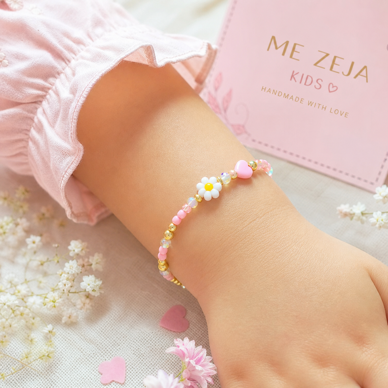 Child’s wrist wearing a pastel flower beaded bracelet beside a pink jewelry box and blossoms