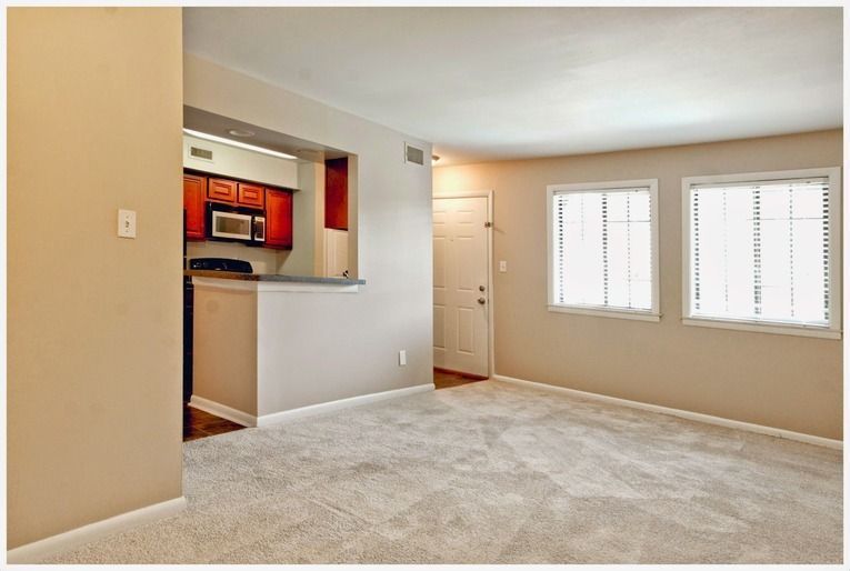 An empty living room with a kitchen in the background