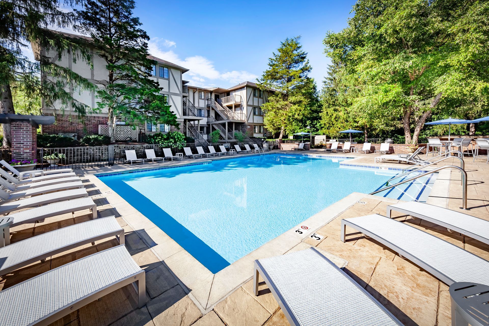 A large swimming pool surrounded by chairs and umbrellas in front of a building.