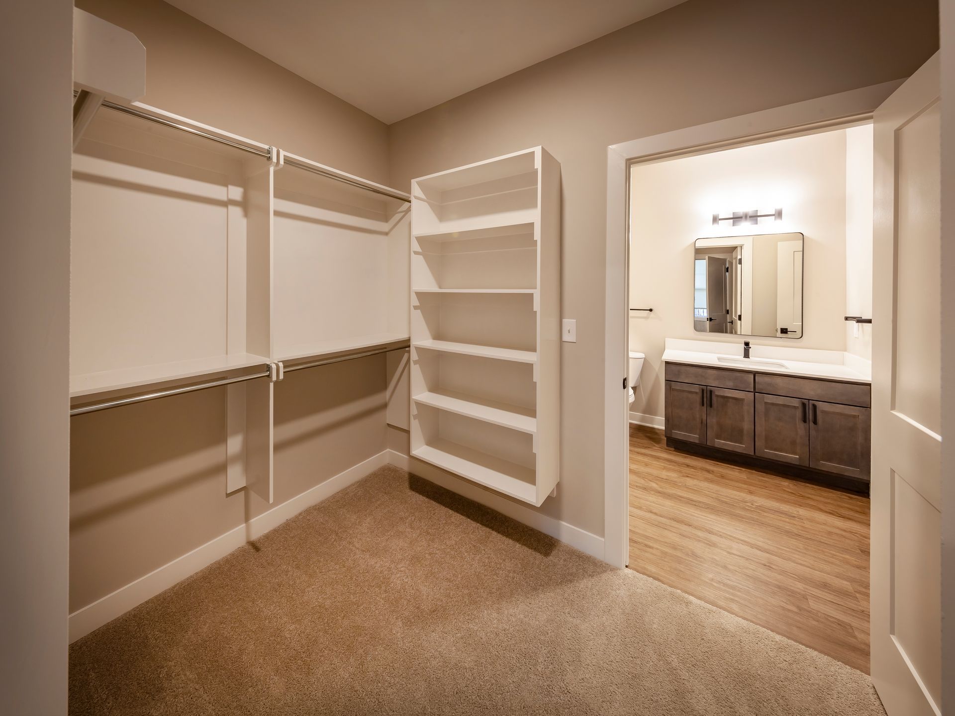A walk in closet with shelves and a bathroom in the background.